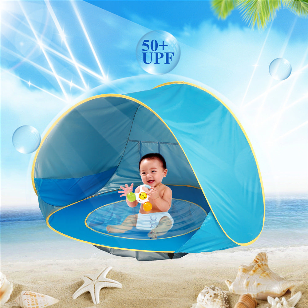 Baby playing under a blue beach tent with 50+ UPF protection on a sunny beach.