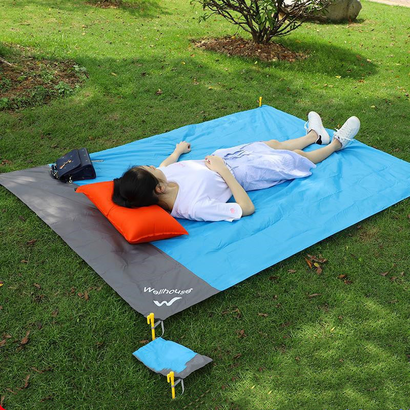 Person lying on a blue and gray mat with an orange pillow in a grassy area.