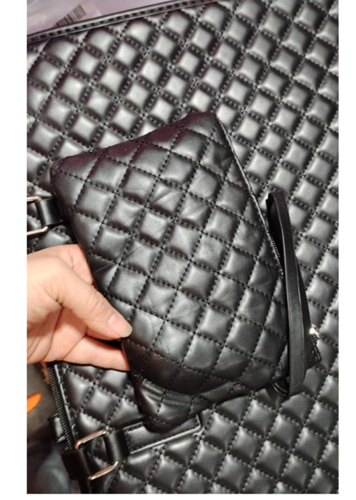 Black quilted handbag with a person's hand holding it against a matching background.