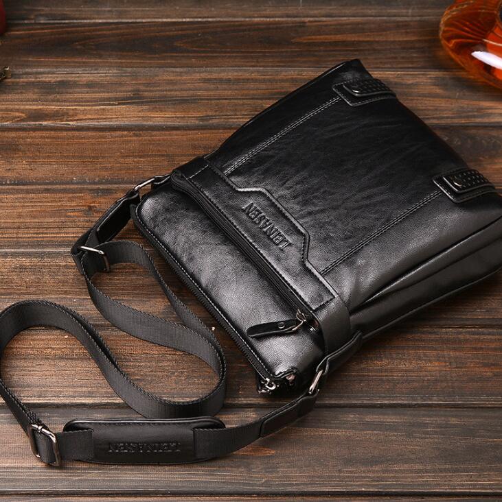 Black leather bag with a strap on a wooden surface.