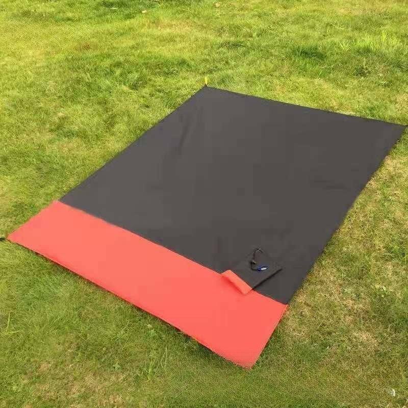 Black and red foldable beach mat on grass.