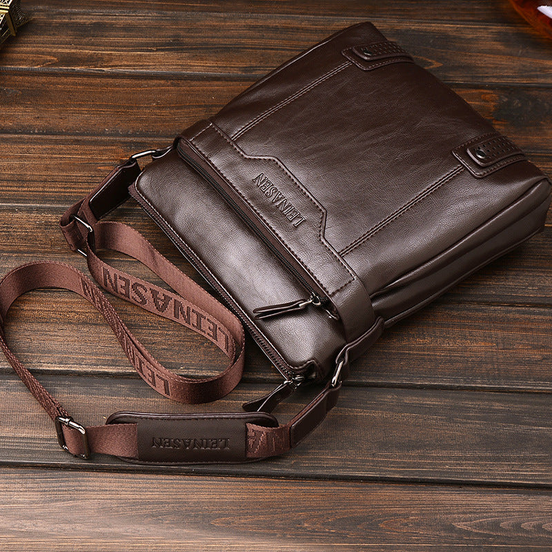 Brown leather bag with strap on a wooden surface.