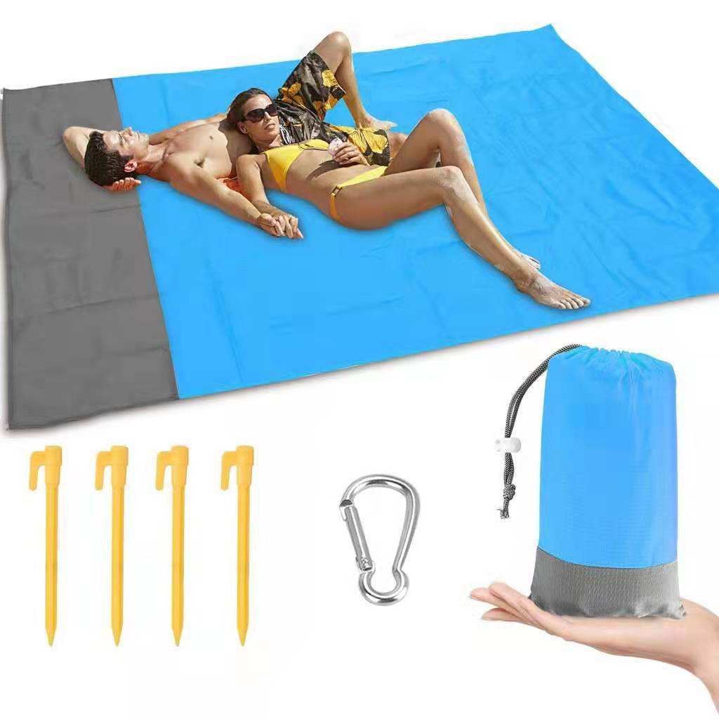 Blue and gray foldable beach mat with people lying on it, surrounded by stakes, carabiner and a folded mat.