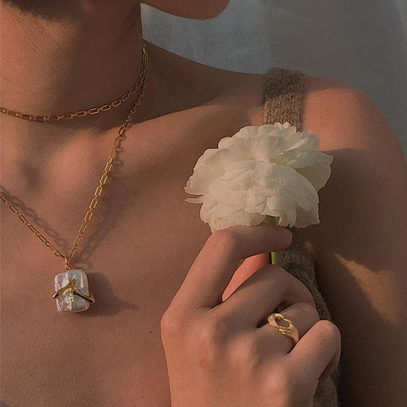 Women wearing a gold necklace and ring, holding a white flower.