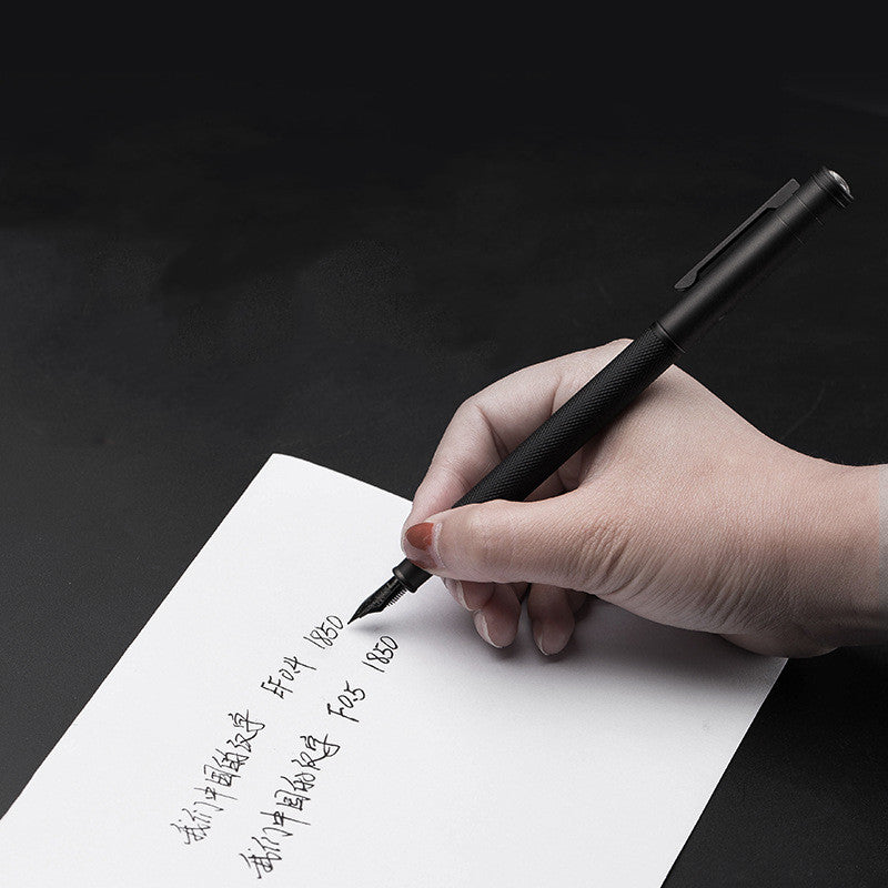 Hand writing on a piece of paper with a black pen against a dark background.