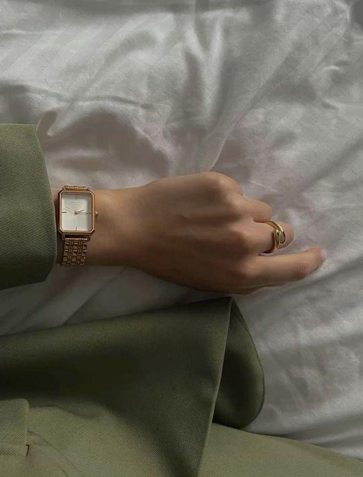 Hand wearing a rose gold watch and ring on a light fabric background.