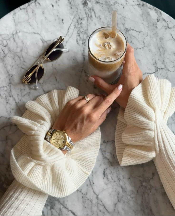 Women holding iced coffee drink on a marble table with sunglasses and watch.