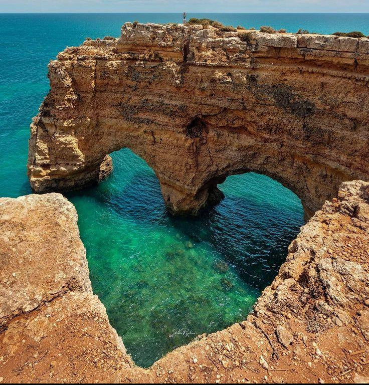 Scenic Algarve coastline with rock and clear ocean water, summer travel atmosphere.