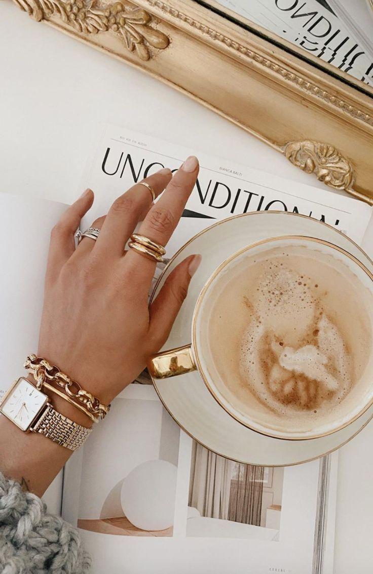 Hand with gold bracelets holding a coffee cup on magazine.