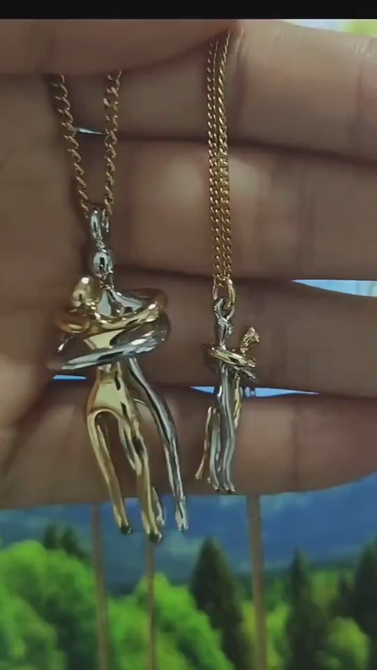 Woman holding and displaying a two-tone hug pendant necklace in her hand, showing a non-tarnish couples necklace design with larger pendant for men and smaller pendant for women.