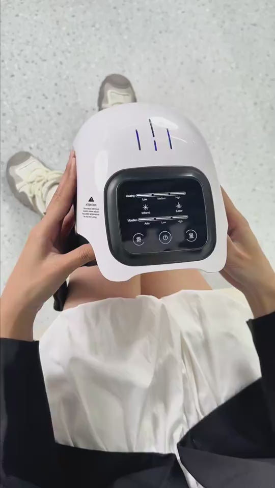 White vibration knee massager shown in a woman’s hand and worn on her knee, demonstrating red light and heat therapy to help relieve knee pain and discomfort related to injury, arthritis, or everyday joint strain.