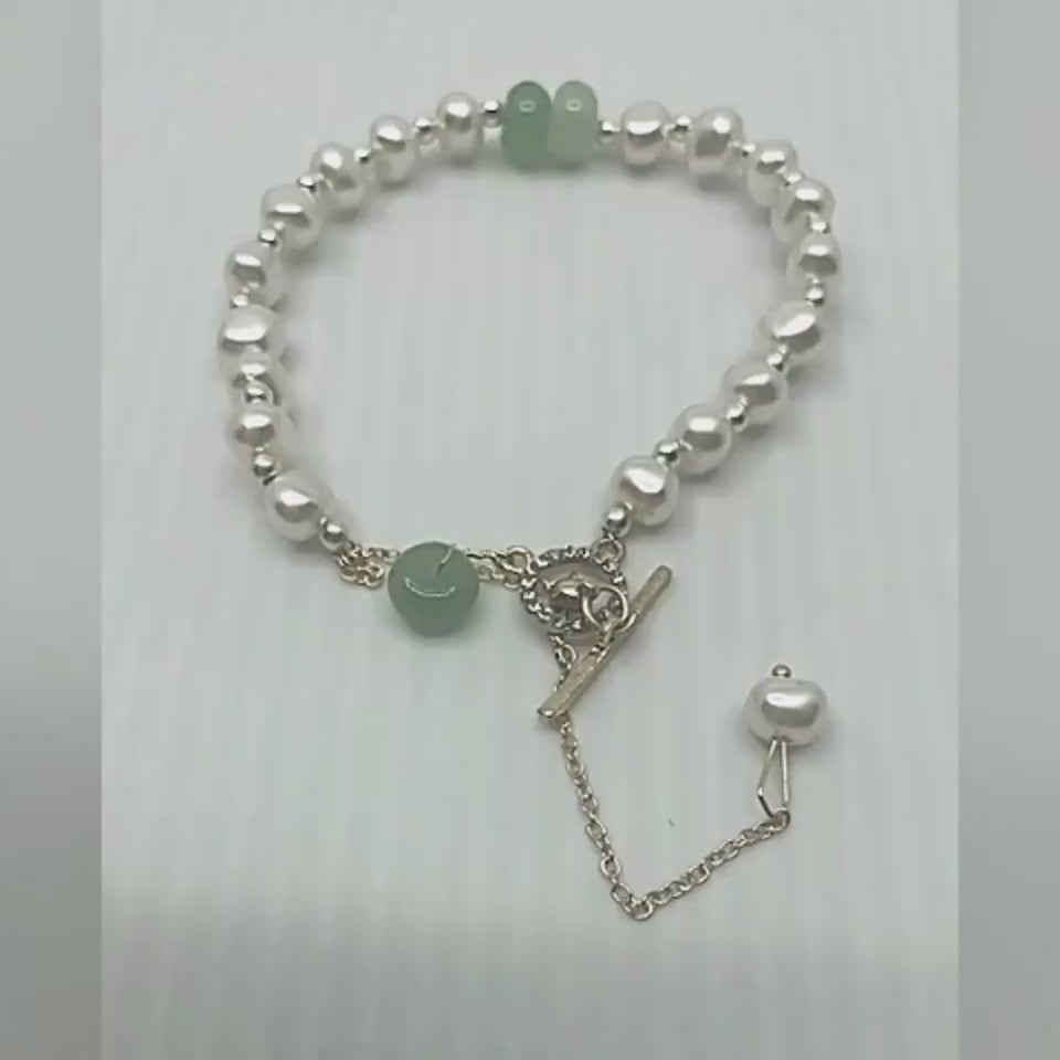 Ultra close-up video of a woman´s hand presenting a women´s necklace, clearly showing the gemstone beads and gold charm with high detail.