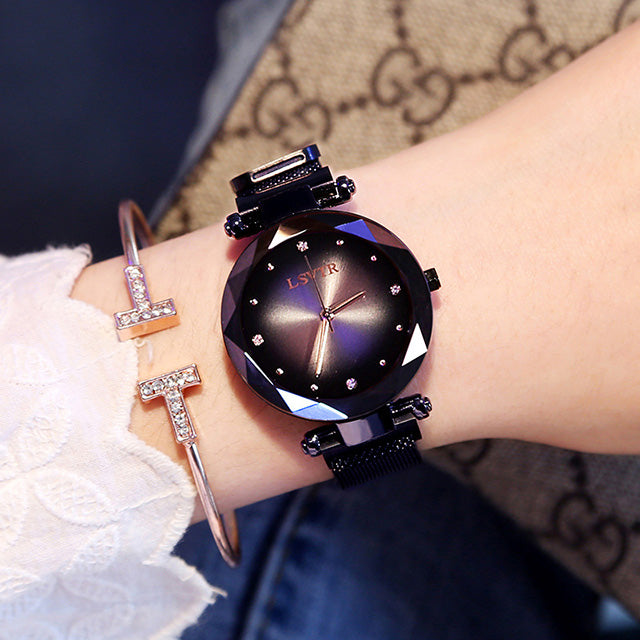 Women´s black watch with geometric dial, worn on wrist and bracelet under bright light.