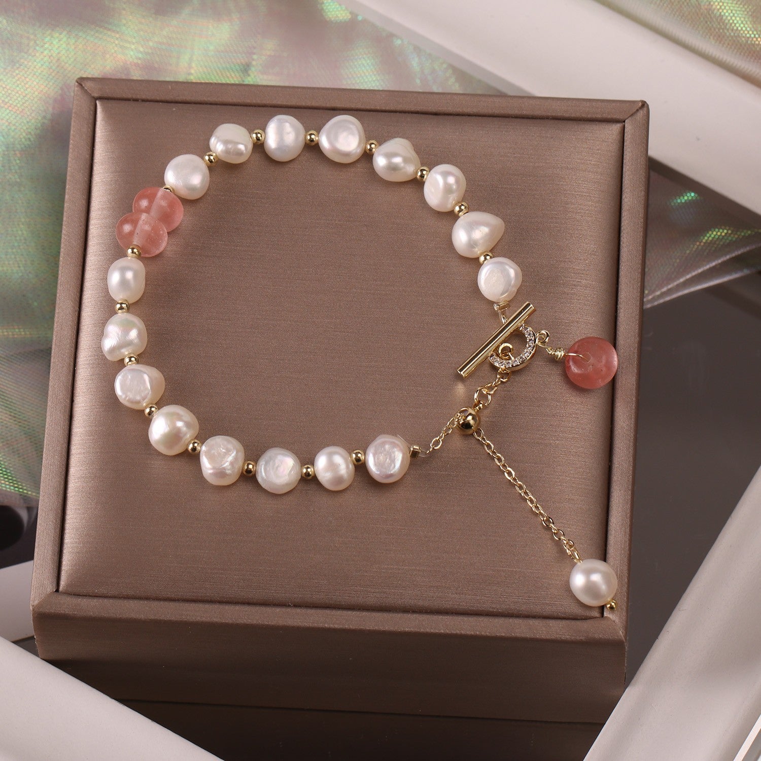 Women´s pearl bracelet with a pink stone on a brown jewelry box.