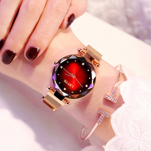 Women´s rose gold watch with red dial, dark-toned geometric bezel and bracelet under bright light.